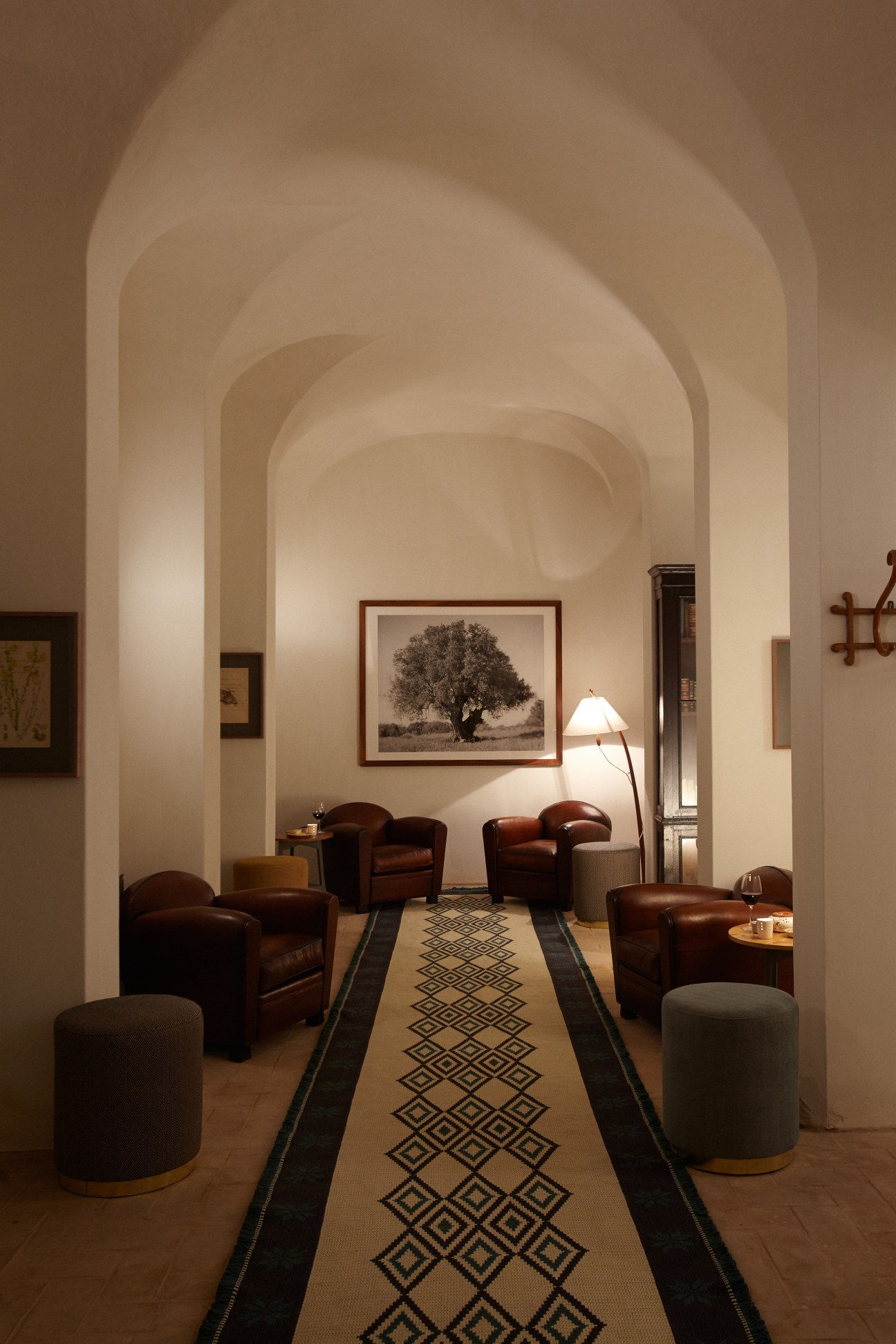 Elegant lounge interior with arched ceilings, leather armchairs, patterned runner rug, and framed artwork.