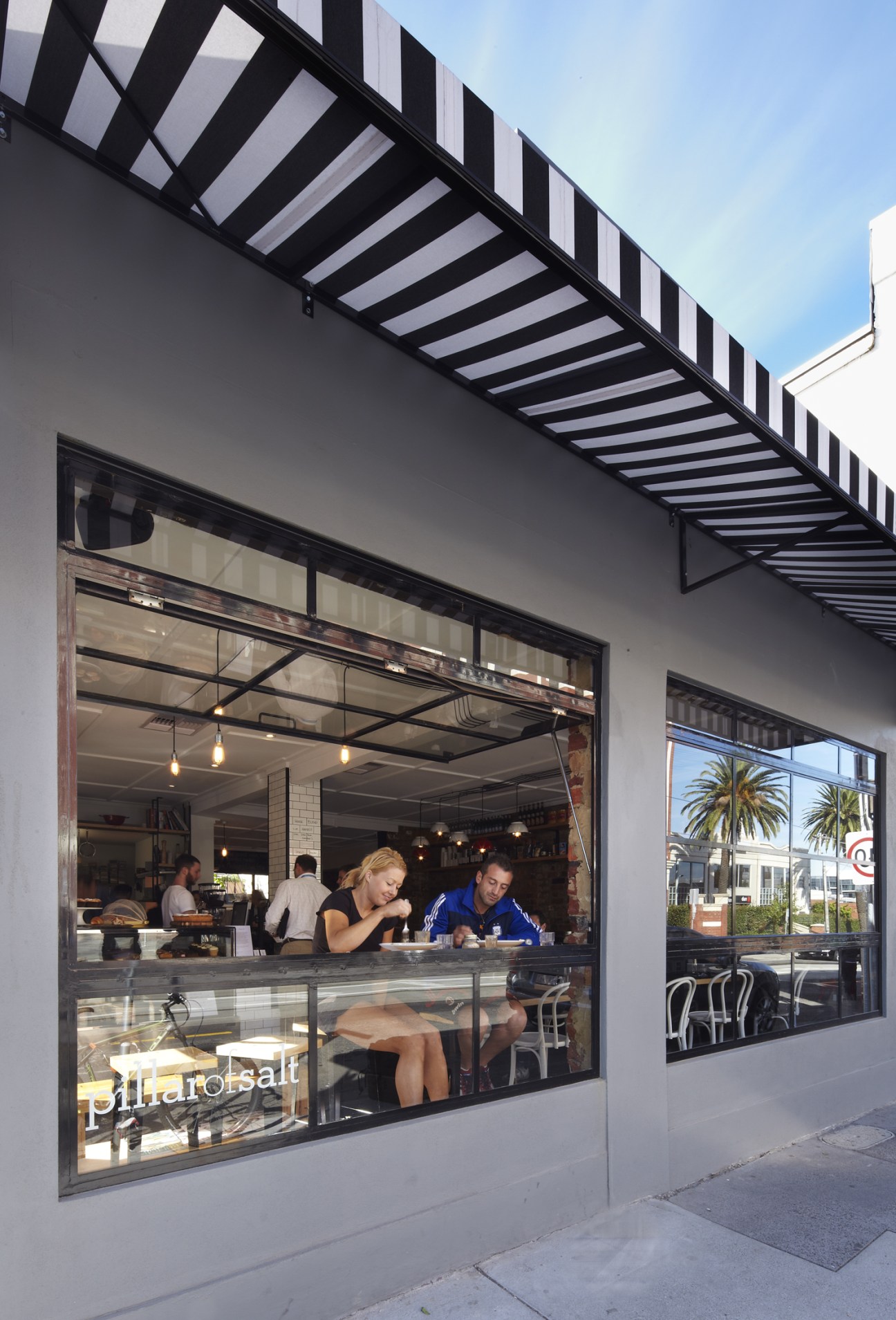 Pillar of Salt café storefront in Melbourne with large windows, striped awning, and customers inside.