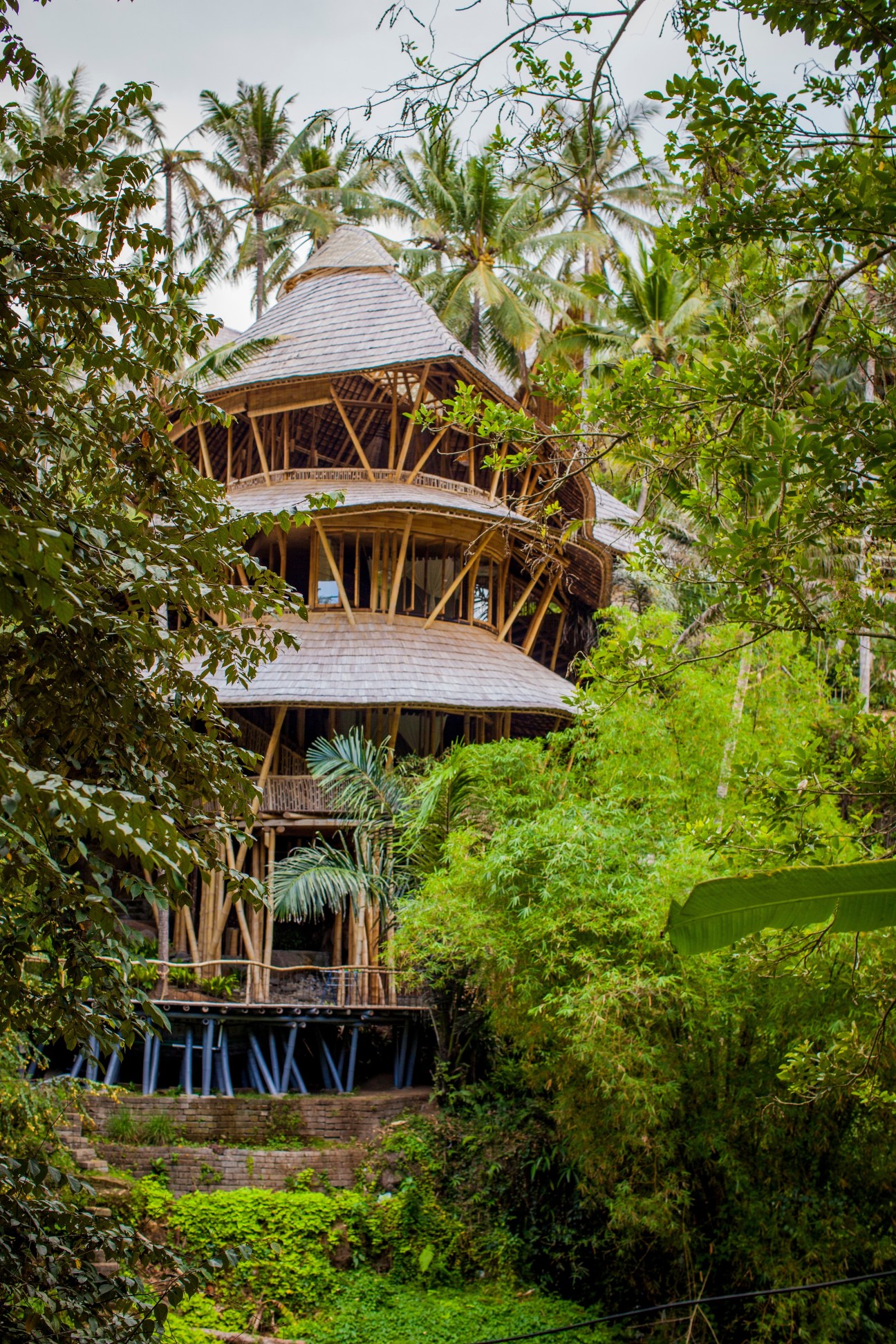 Bamboo tower structure with curved architecture nestled among lush green tropical vegetation and palm trees in Bali.