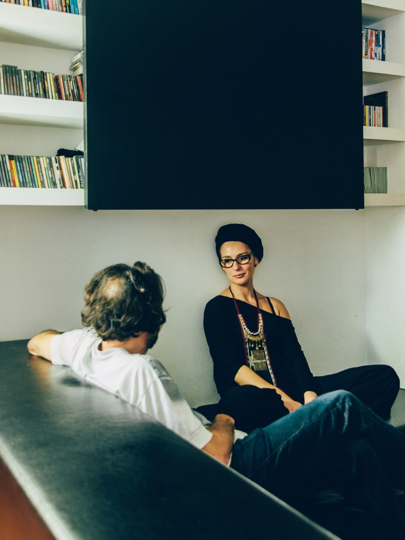 Two people sitting against a white wall with built-in bookshelves in a modern apartment interior.