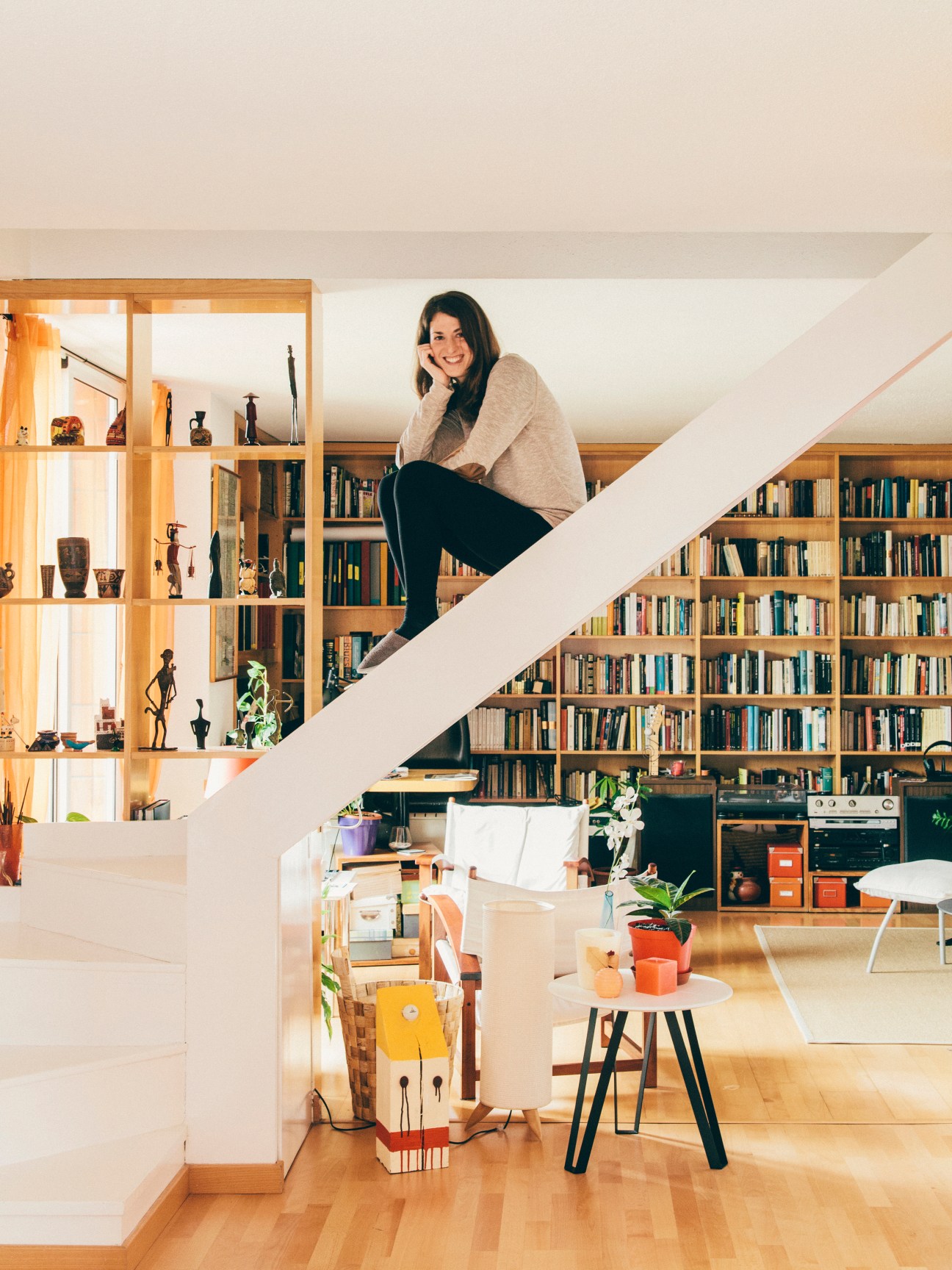 Woman sitting on white staircase in modern apartment with wooden shelving and bookshelves.