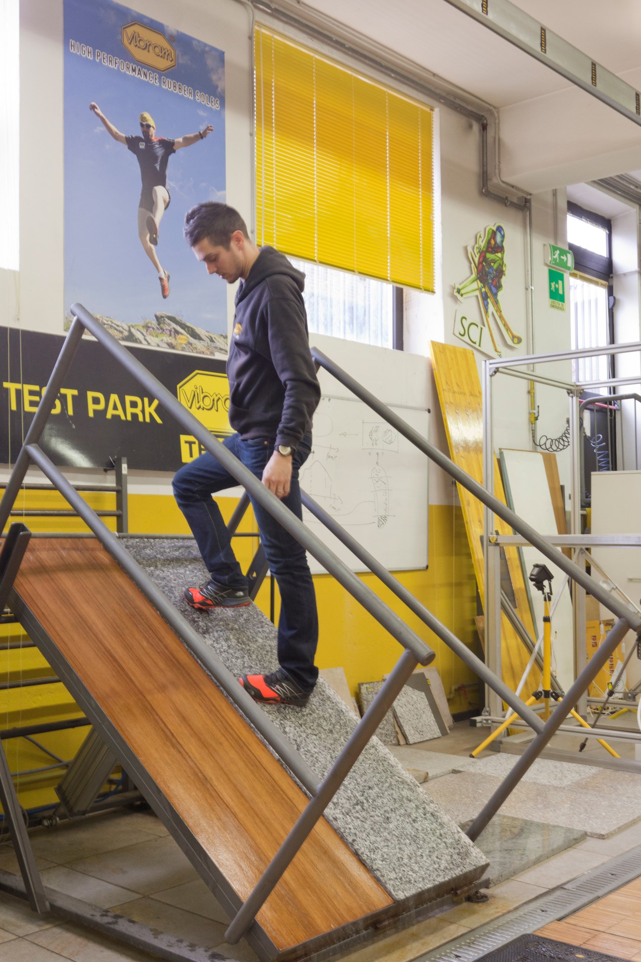 Man descending wooden and rubber-surfaced stairs in Vibram test facility with yellow branding visible.