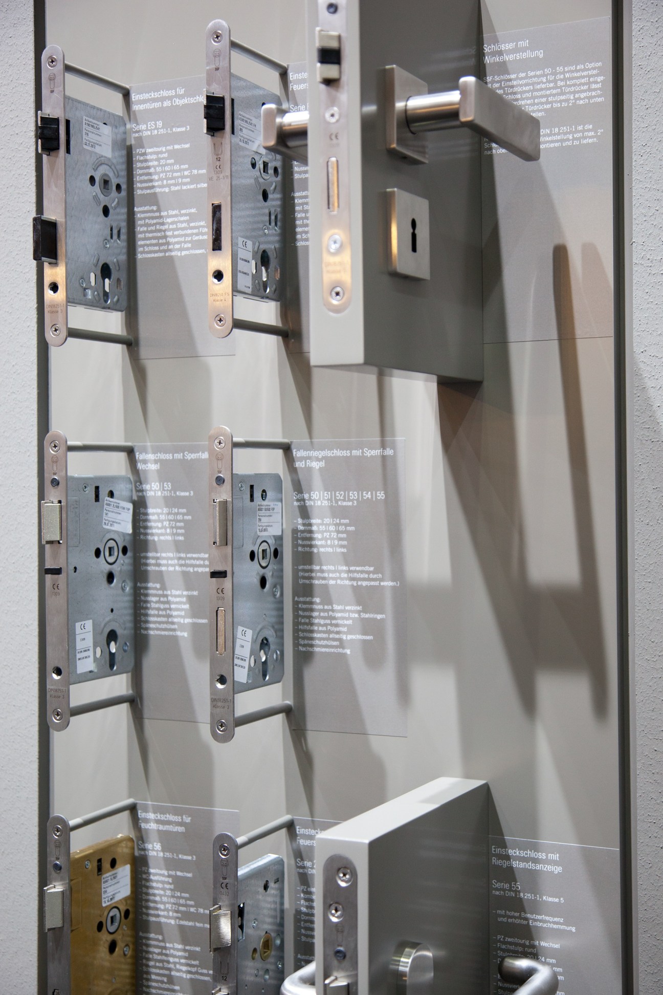 Display of various stainless steel door locks and locking mechanisms with technical specifications mounted on white panels.