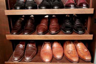 Multiple pairs of John Lobb leather shoes displayed on wooden shelves in various shades of brown and burgundy.