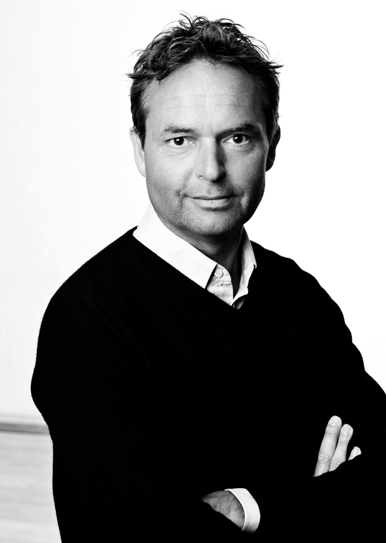 Black and white portrait of a man in a dark sweater and white shirt against a light background.