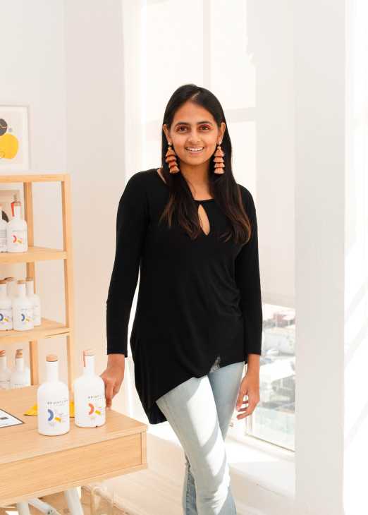 Aishwarya Iyer, founder of Brightland olive oil, standing in her showroom with products displayed on wooden shelving.