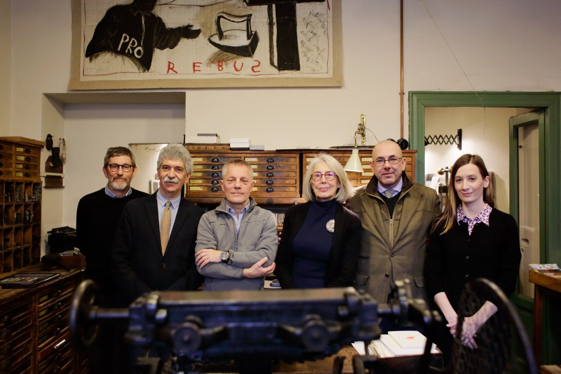 Six people stand together inside Fratelli Bonvini stationery shop with wooden storage drawers visible behind them.