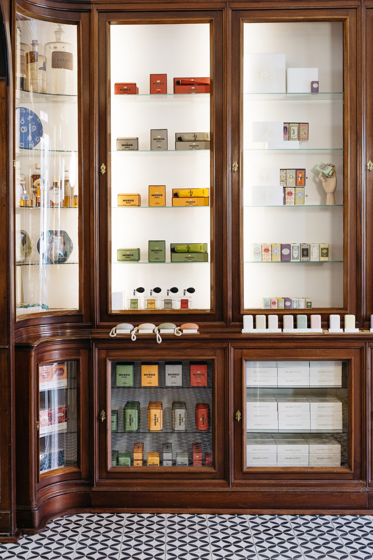Claus Porto flagship store interior with wooden display cabinets featuring colorful packaged soaps and beauty products organized on glass shelves.