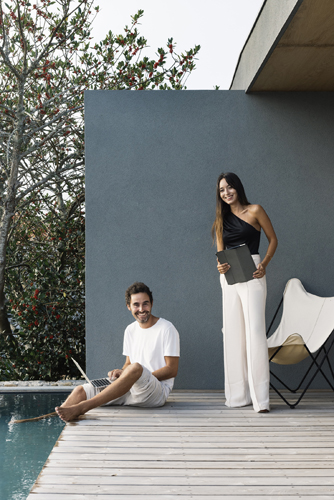 Two people relax by a swimming pool on a modern office terrace with grey wall and wooden deck.