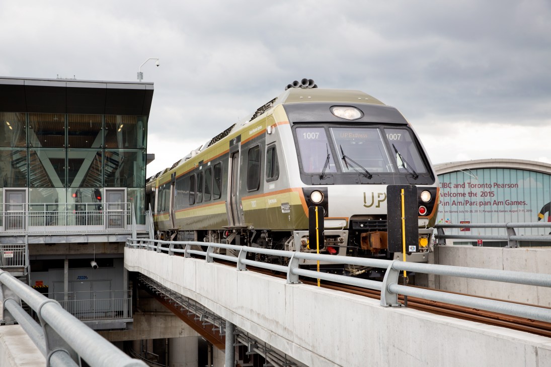 UP Express train with sage green and pumpkin orange livery parked at station platform.