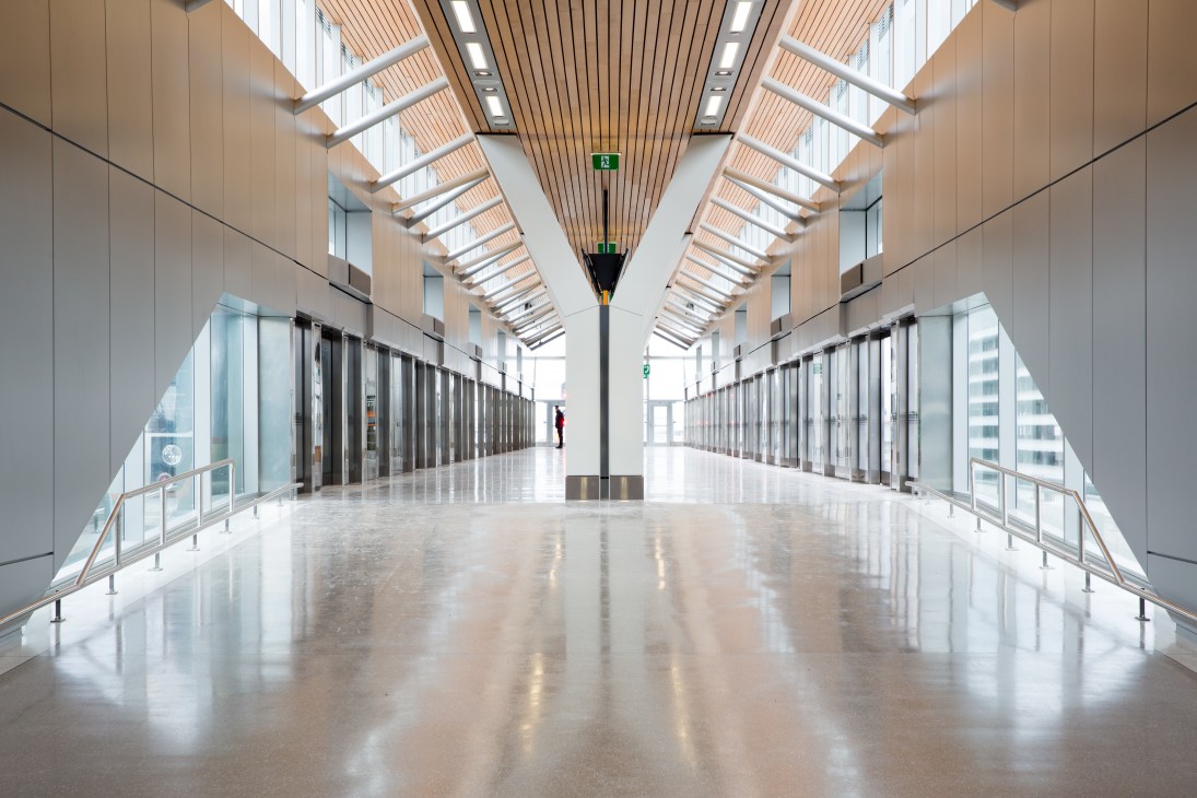 UP Express station platform with ribbed-oak ceiling beams, terrazzo flooring, and natural light filtering through skylights.