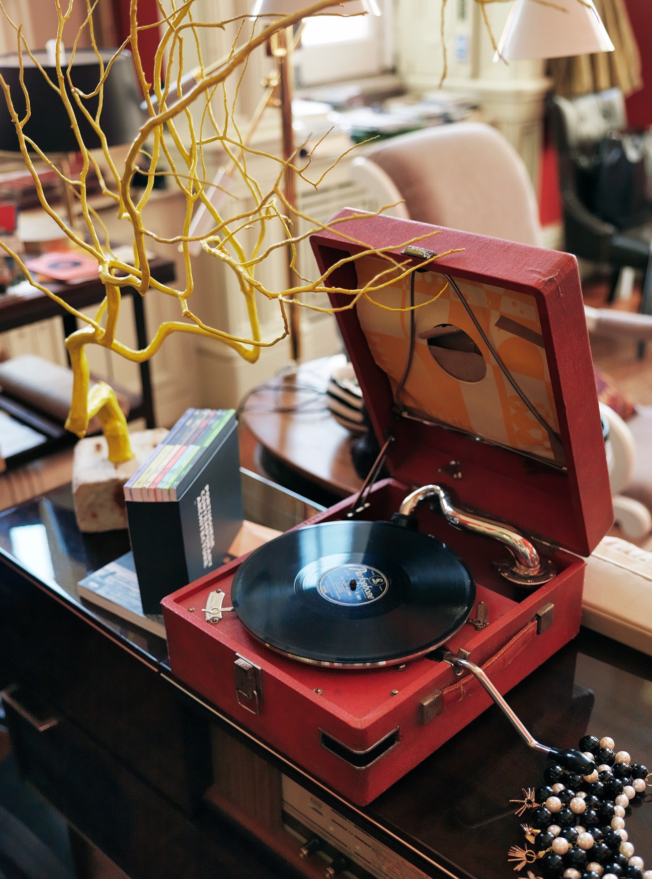 Red vintage record player with vinyl record, decorative gold branches, and beaded necklace on display shelf.