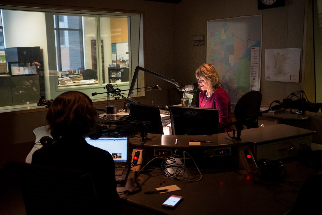 Two women in a radio studio during a broadcast, sitting at a desk with microphones and computer equipment.
