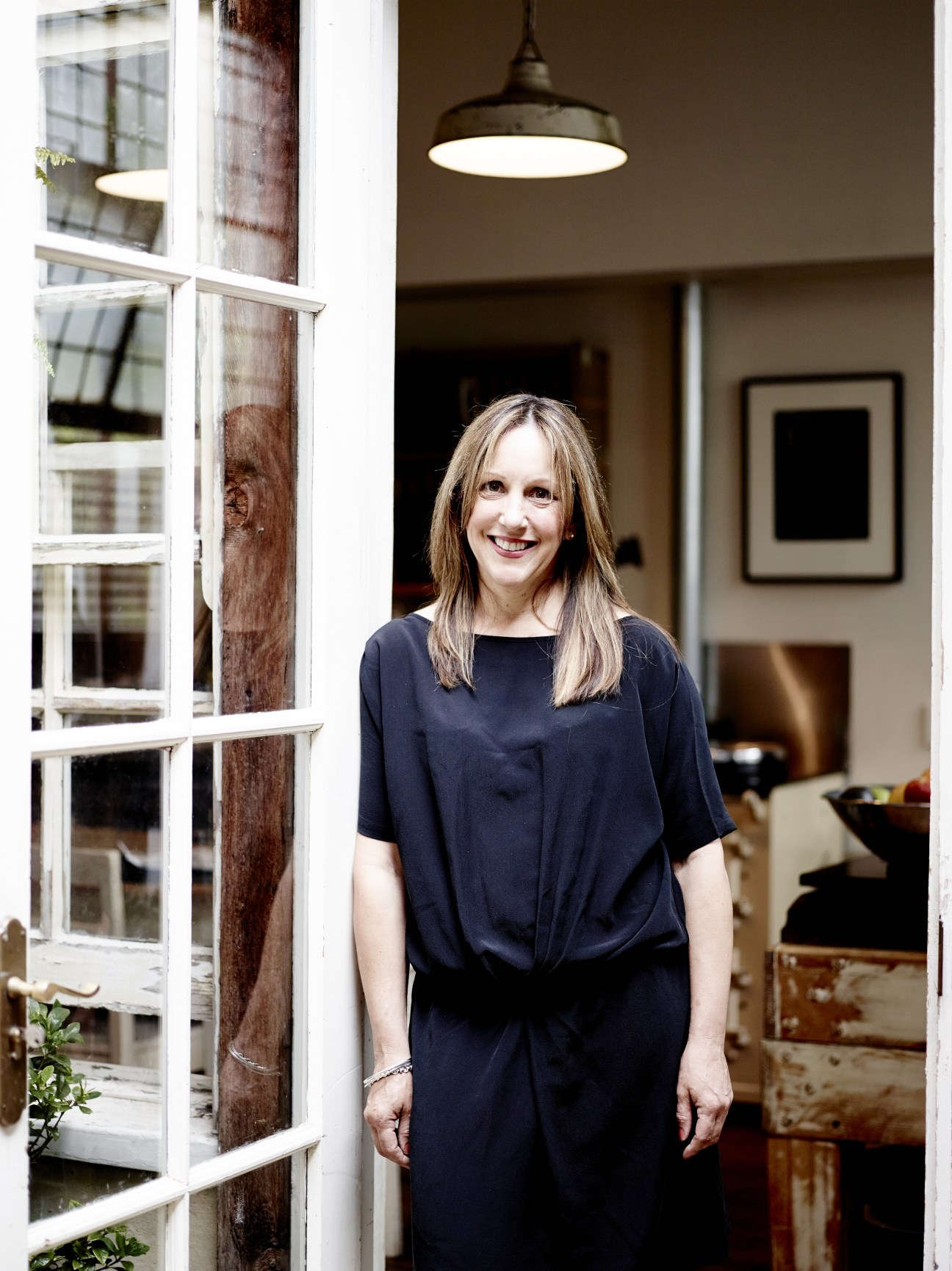 Artist Adriane Strampp standing in her renovated Collingwood apartment with industrial pendant light and large windows.