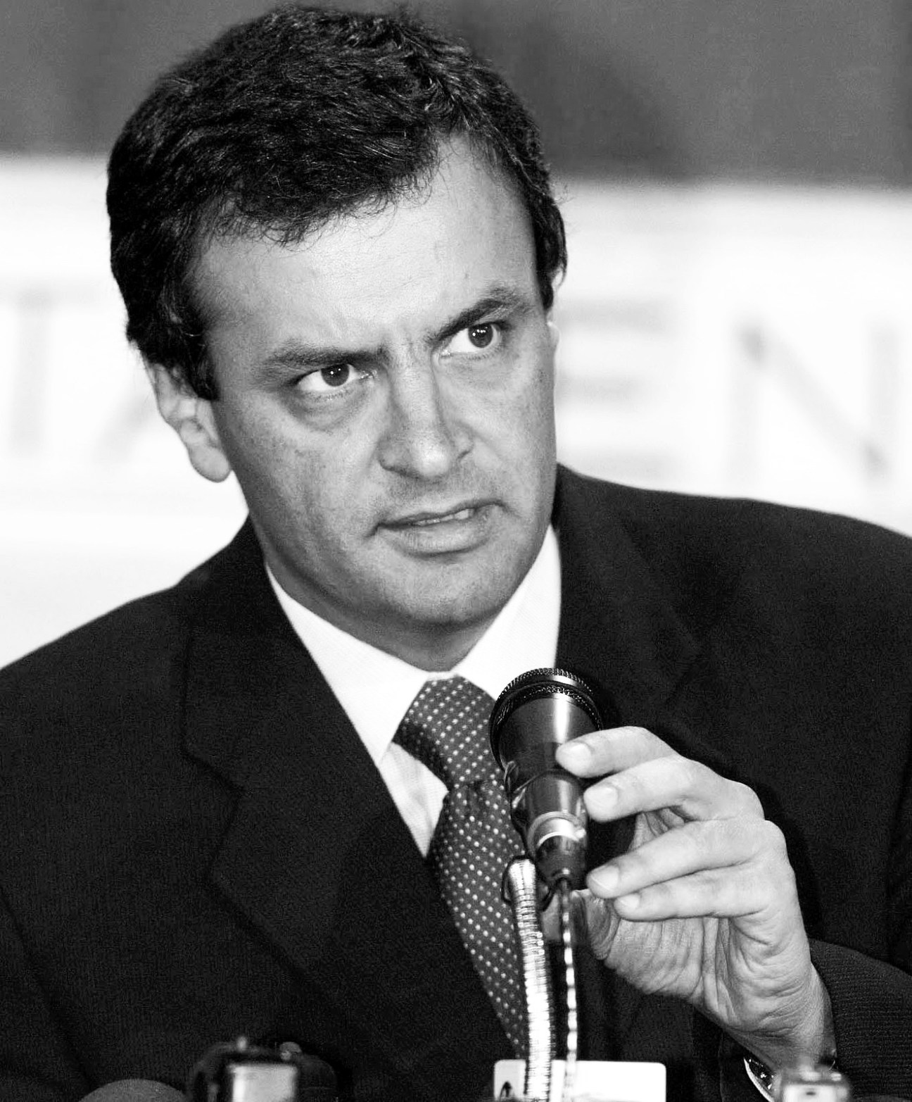 Black and white portrait of a man in a dark suit holding a microphone.