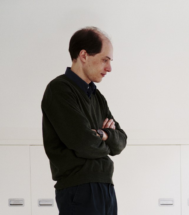 Man in dark sweater standing with arms crossed against white wall