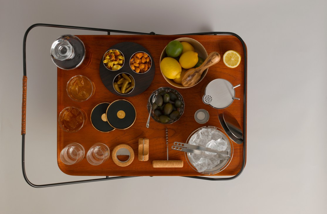 Overhead view of a wooden drinks trolley with bartending tools, glassware, garnishes and cocktail accessories arranged neatly.