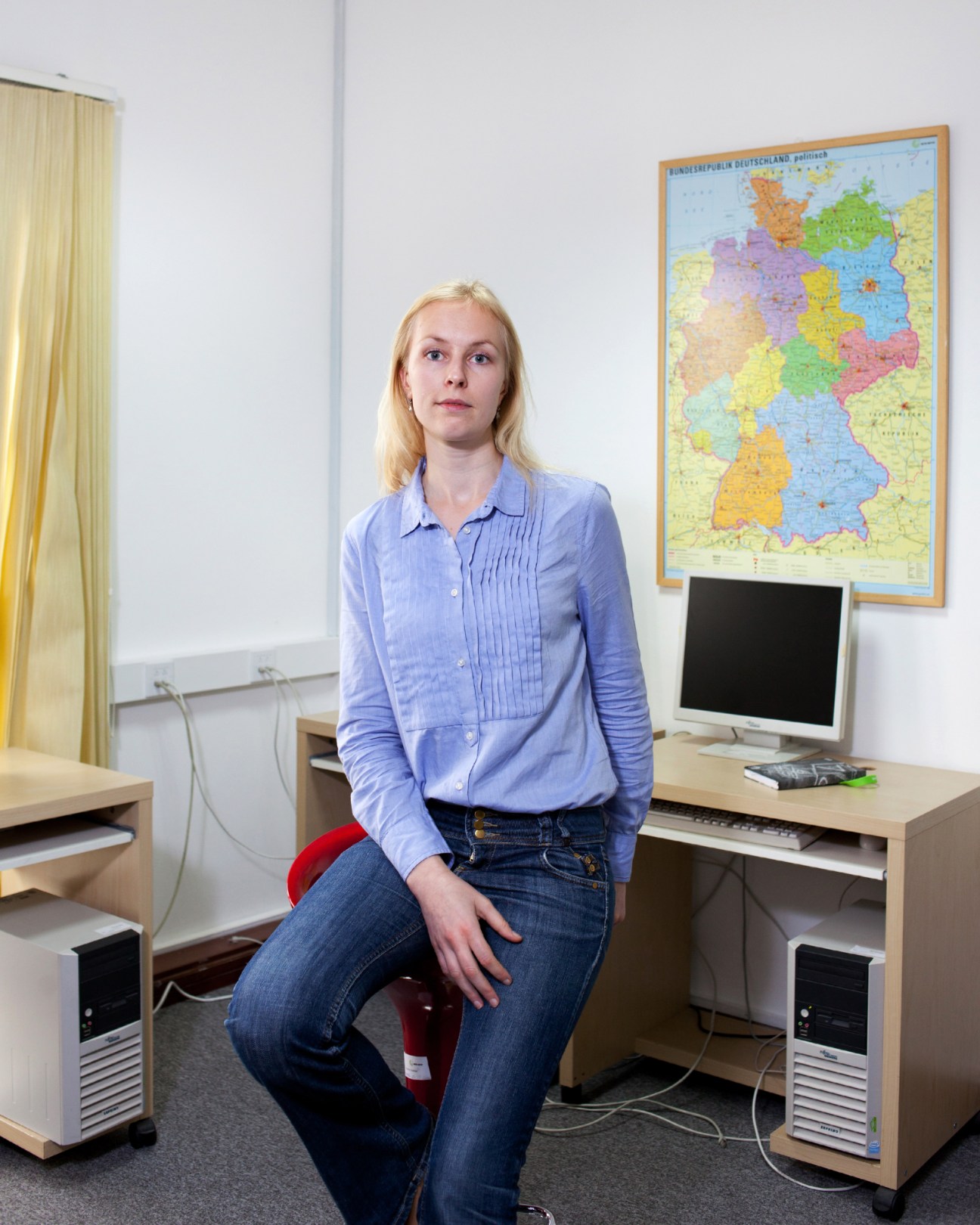 Annegret Steudner, German language teacher at the Goethe Institut, sitting at a desk in a classroom with a colorful map of Germany on the wall behind her.