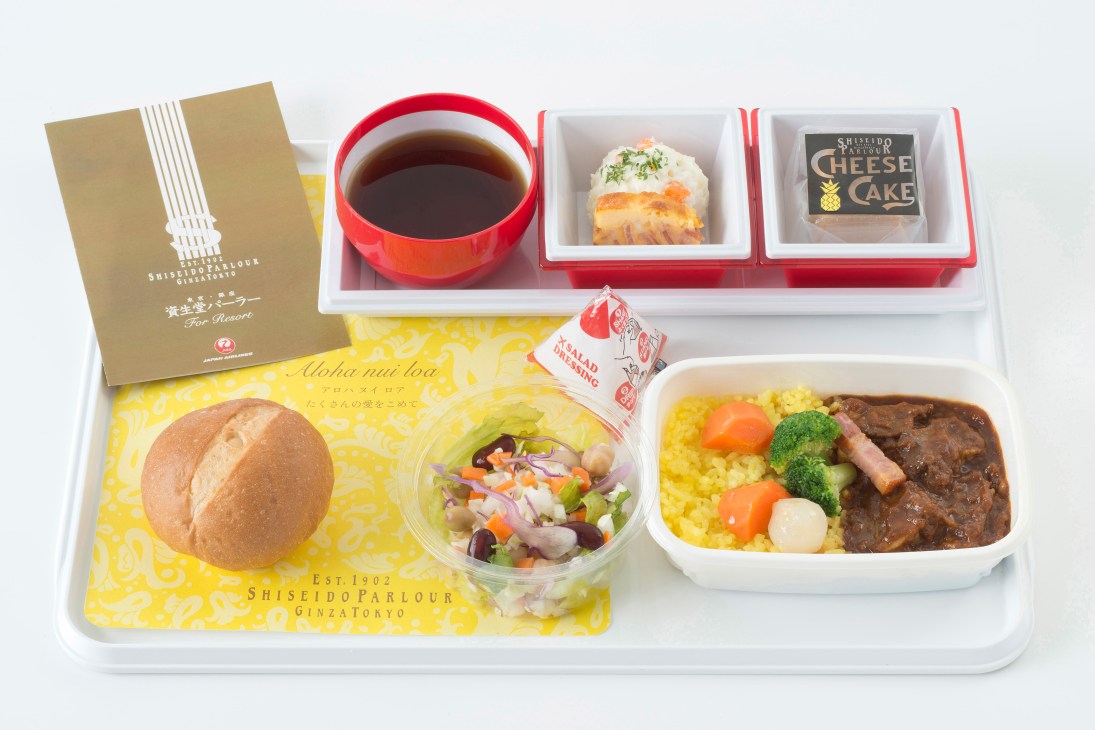 JAL Economy Class meal tray featuring Shiseido Parlour yoshoku dishes including beef stew, bread roll, salad, and desserts with beverage.