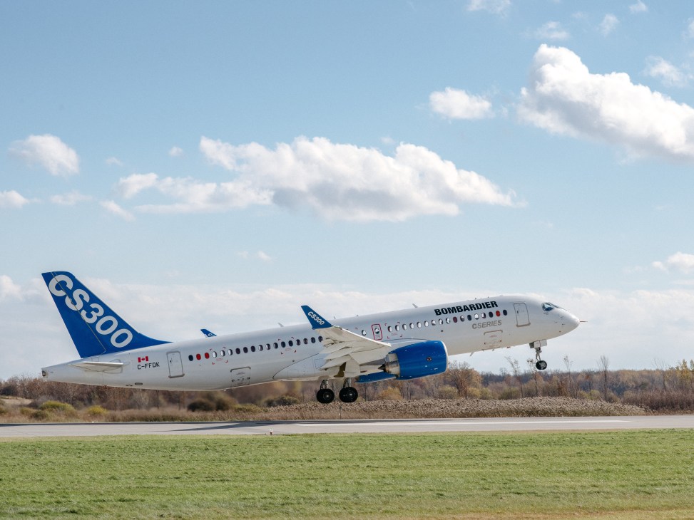 Bombardier C Series aircraft taking off with blue sky and clouds.