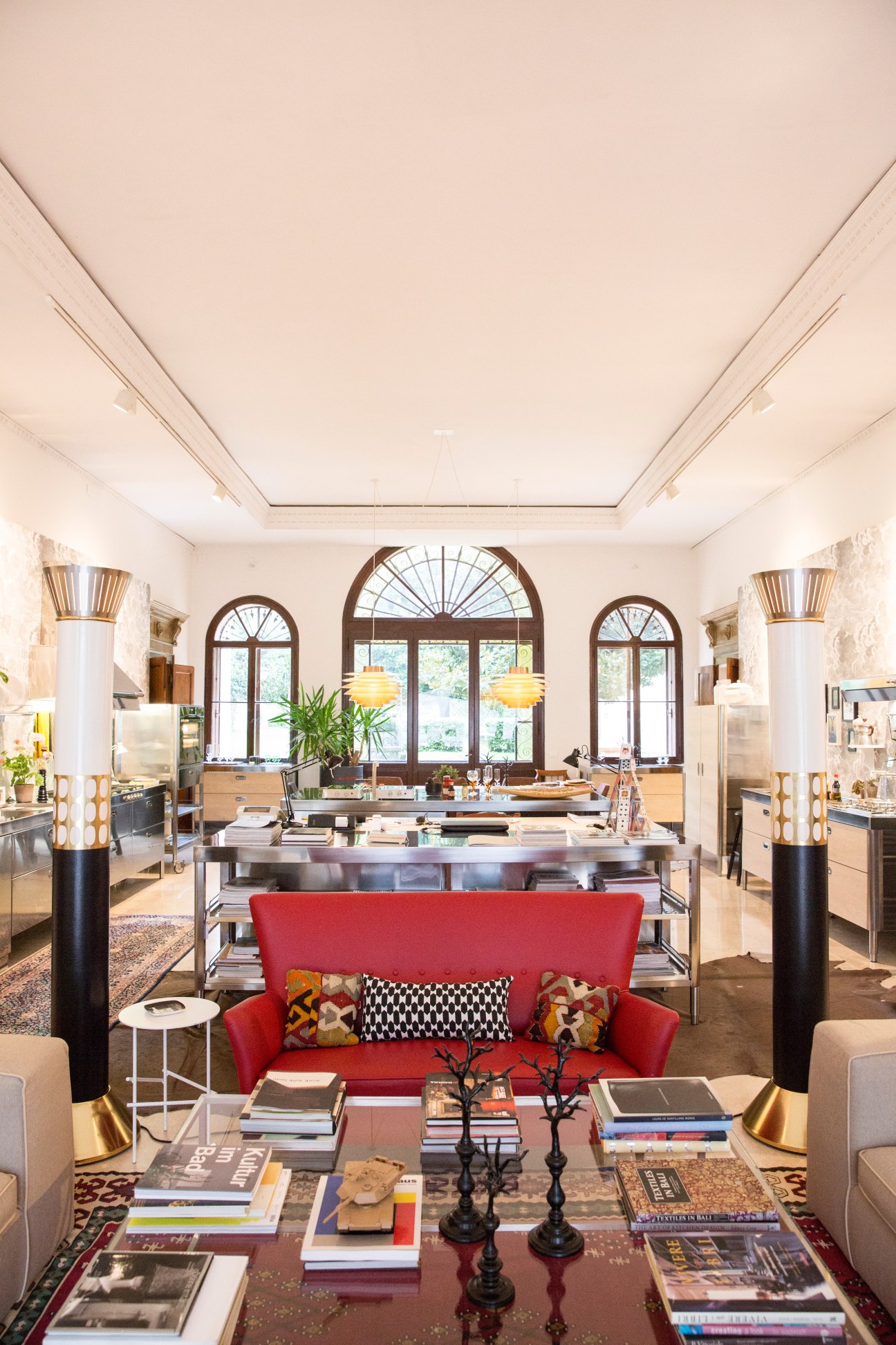Modern kitchen showroom with red sofa, stainless steel counters, arched windows and pendant lighting.