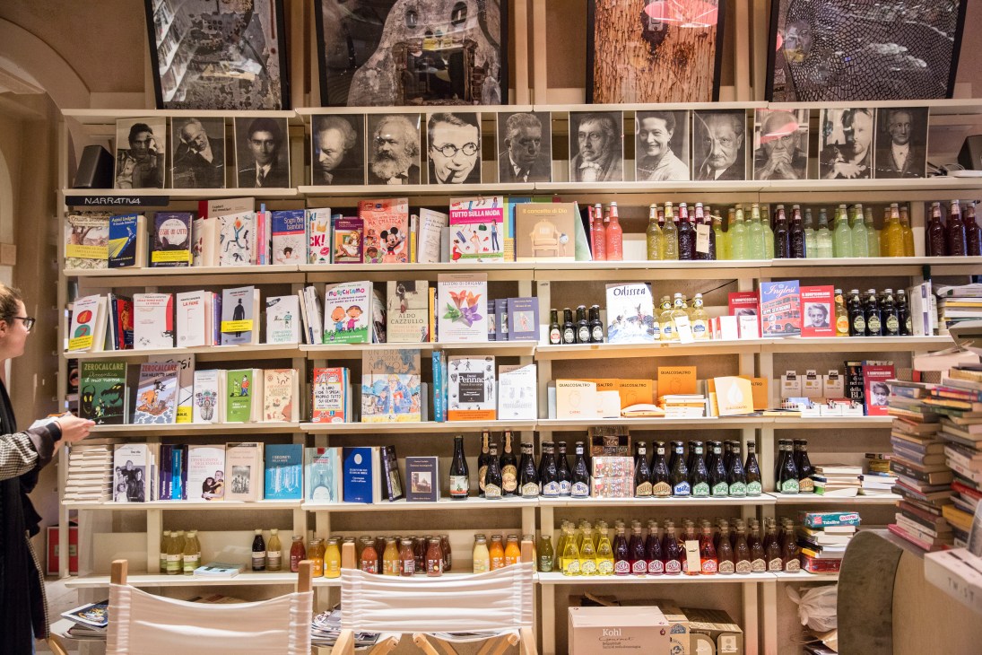 Interior of Caffé dei Libri bookshop with shelves displaying books, beverages, and portraits of philosophers on the wall.