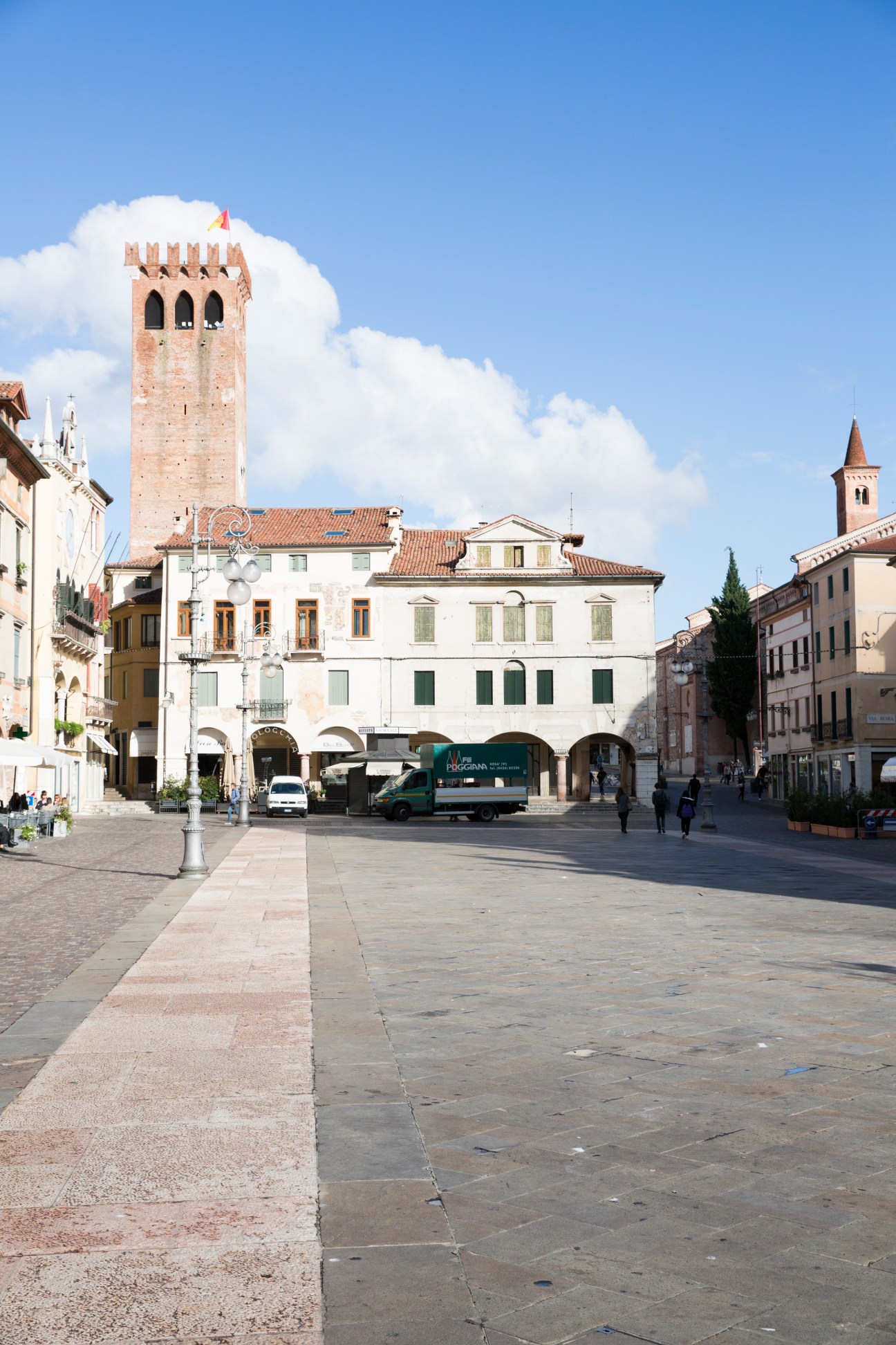 Piazza Libertà in Bassano del Grappa with medieval tower and historic buildings under blue sky.