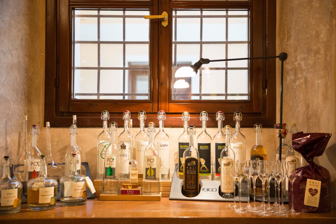 Bottles of Poli grappa displayed on a wooden counter with glasses and period lighting.