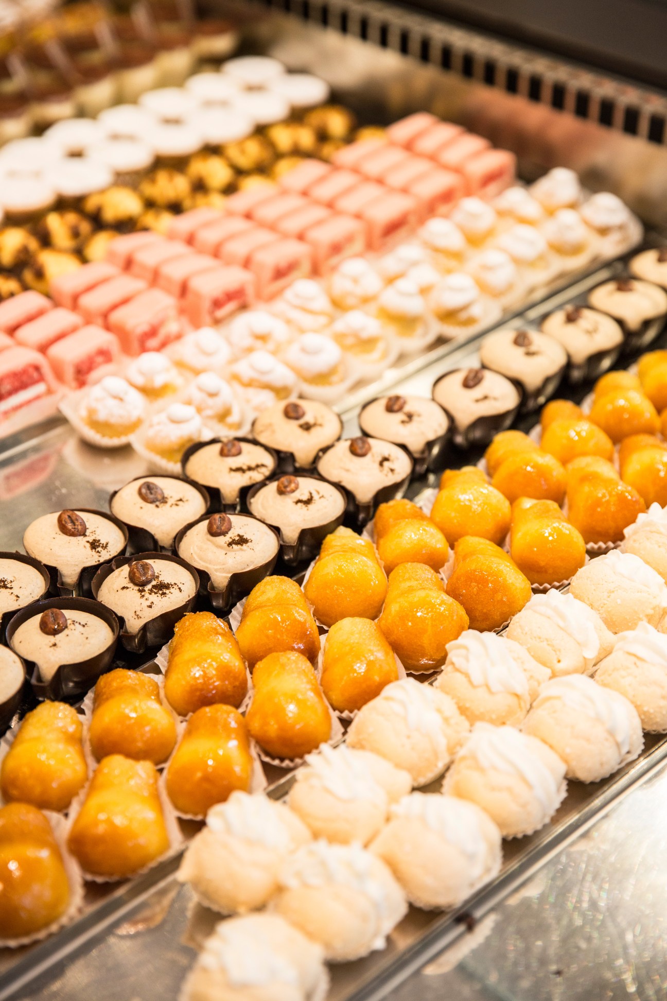 Display case of colorful pastries and confections at Dolce Bassano patisserie, including macarons, chocolate-topped meringues, and glazed candies.