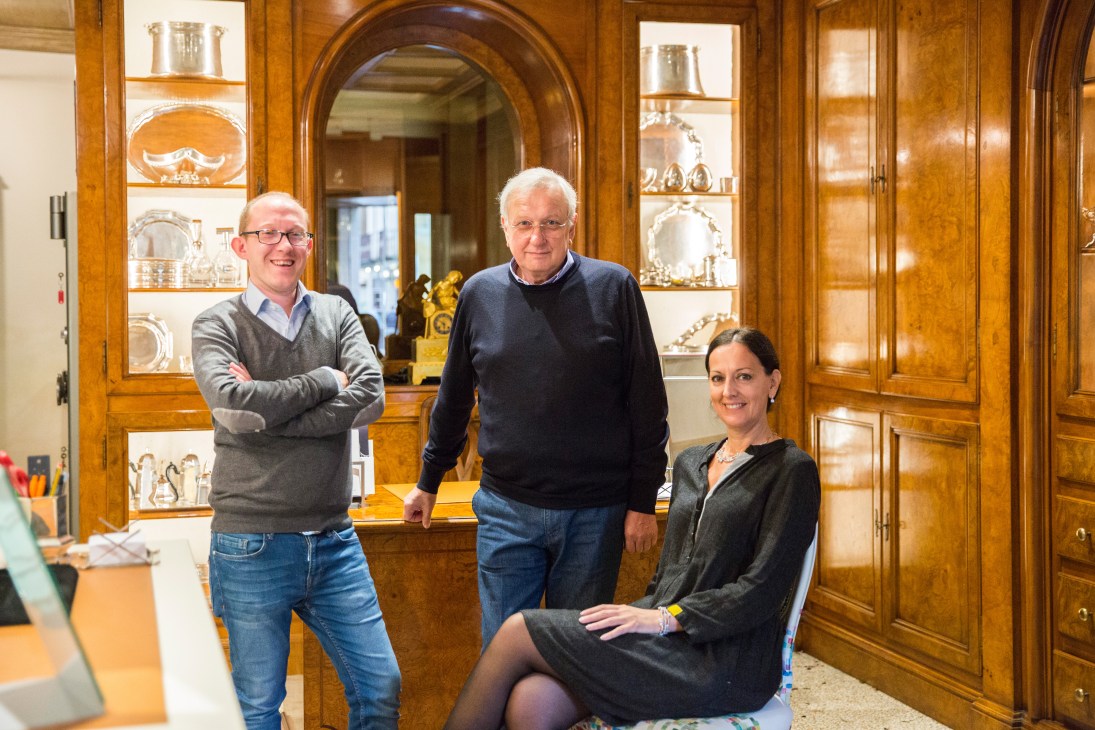 Three people posing in Favero jewellery shop with wooden display cabinets behind them.