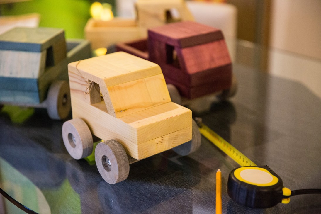 Handcrafted wooden toy trucks and vehicles in natural wood tones displayed on a work surface.