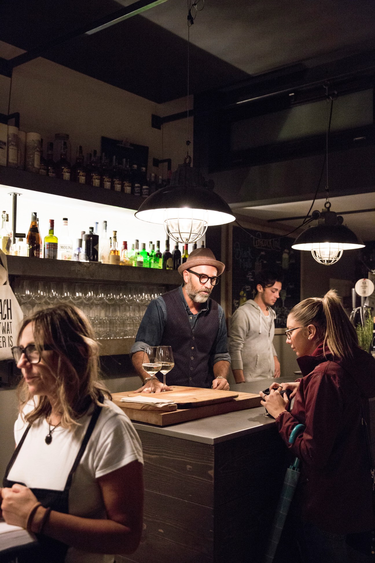 Customers enjoying drinks at Tipic bar in Bassano, with a bartender serving wine behind the counter.