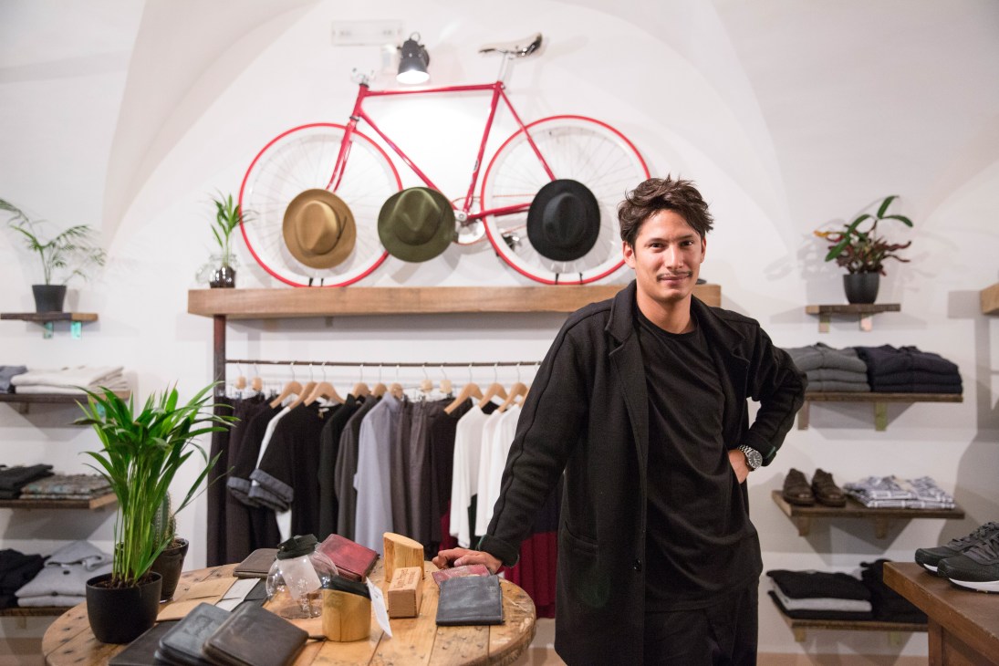 Man standing in Wooden fashion store with red bike and hats displayed on wall.