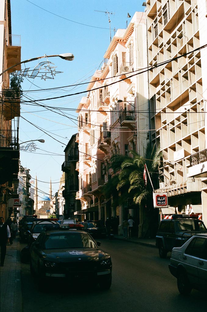 Street view of Gemmayzeh in Beirut with French Mandate-era architecture, palm trees, and parked cars under clear sky.