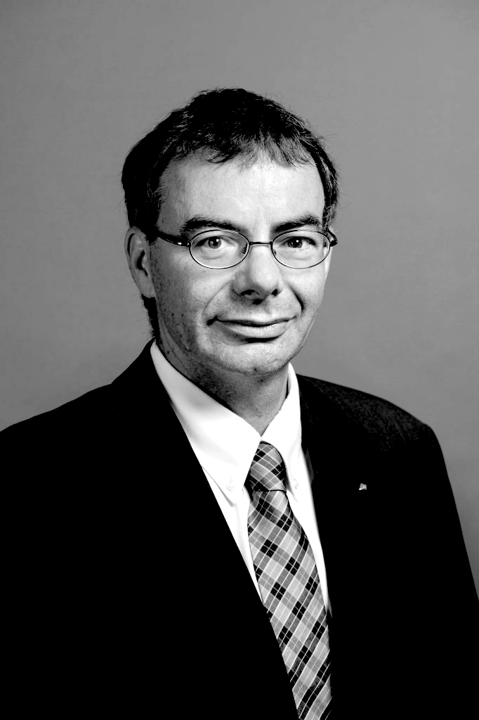 Black and white portrait of Thomas Bieger, Chairman of CEMS, wearing glasses and a suit with plaid tie.