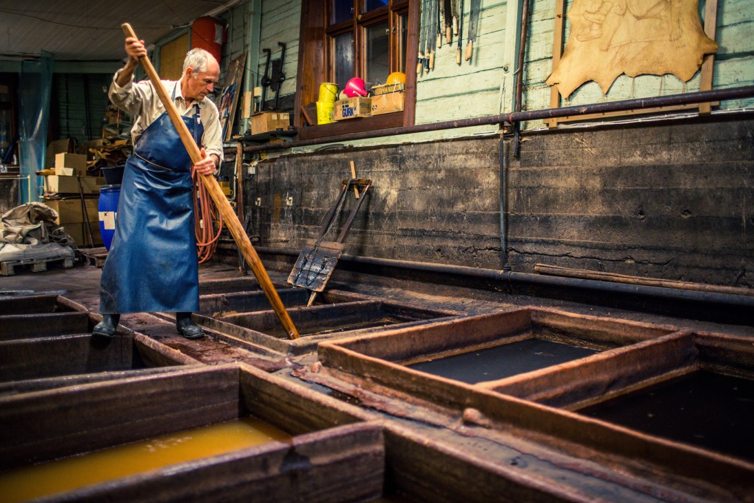 A craftsman in a blue apron stirs leather hides in traditional tanning vats at Böle tannery in Sweden.