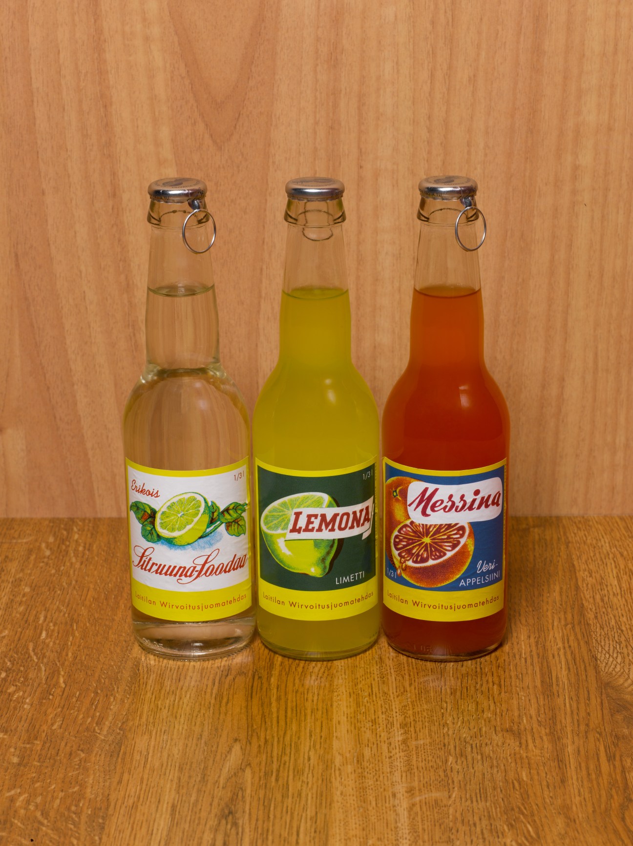 Three vintage Finnish Laitilan soda bottles with lemon, lime and blood-orange flavours on wooden surface.