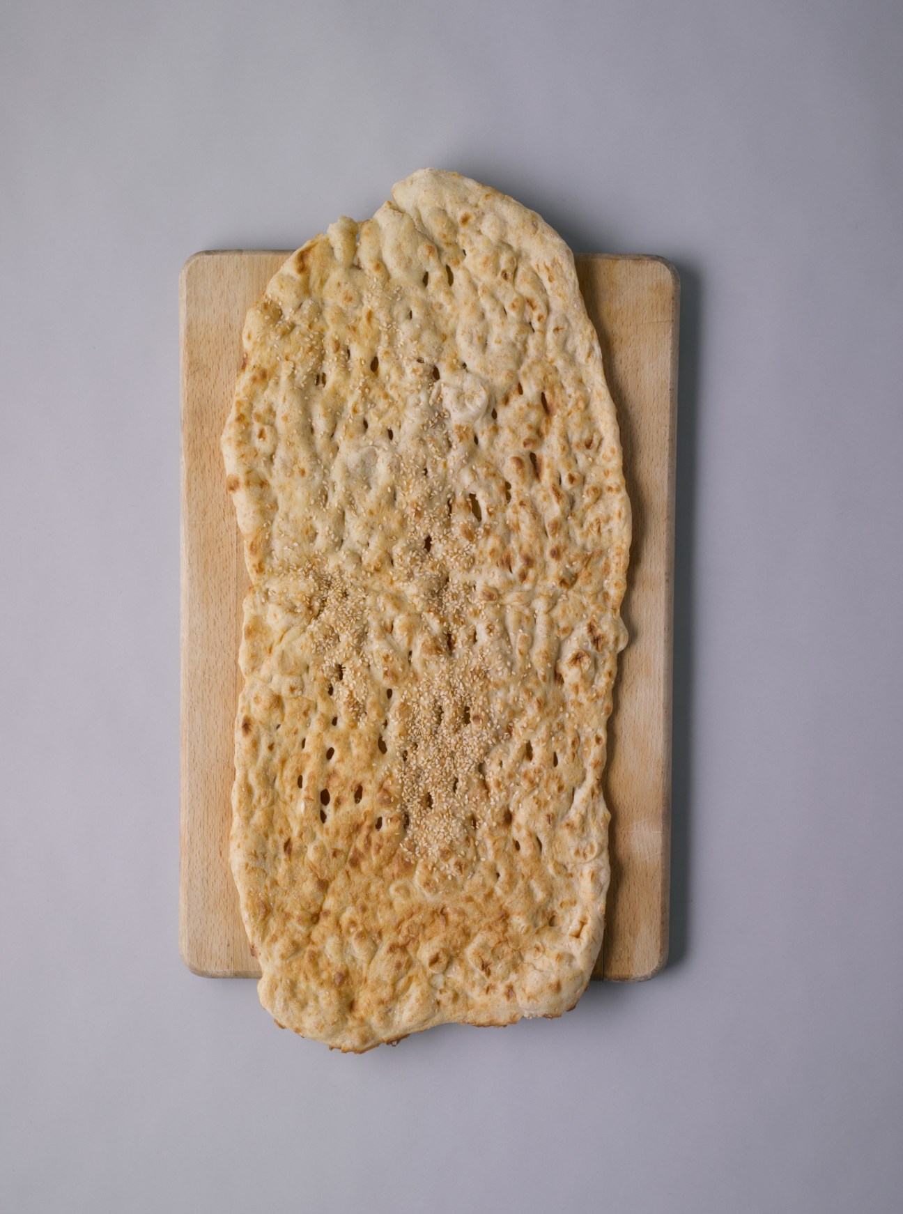 Sangak flatbread on a wooden board, showing its porous texture and sesame seed topping.