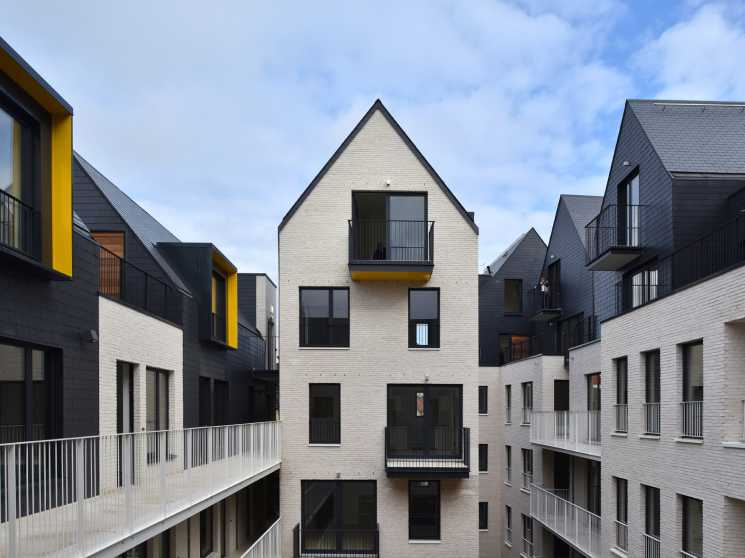 Modern residential buildings with white brick facades, pitched slate roofs, and yellow accent frames surrounding a central courtyard in Brussels.