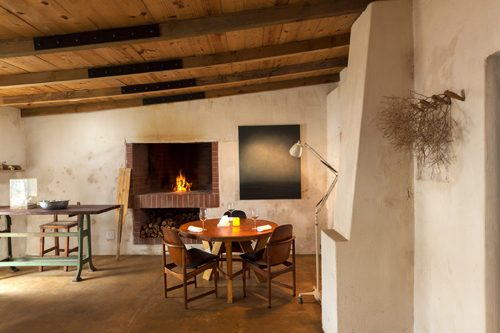 Interior of Wolfgat restaurant with wooden beams, fireplace, dining table and chairs in a whitewashed cottage.