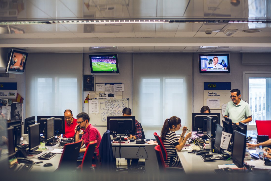 Cadena SER broadcast control room with staff at desks and monitors displaying television feeds.