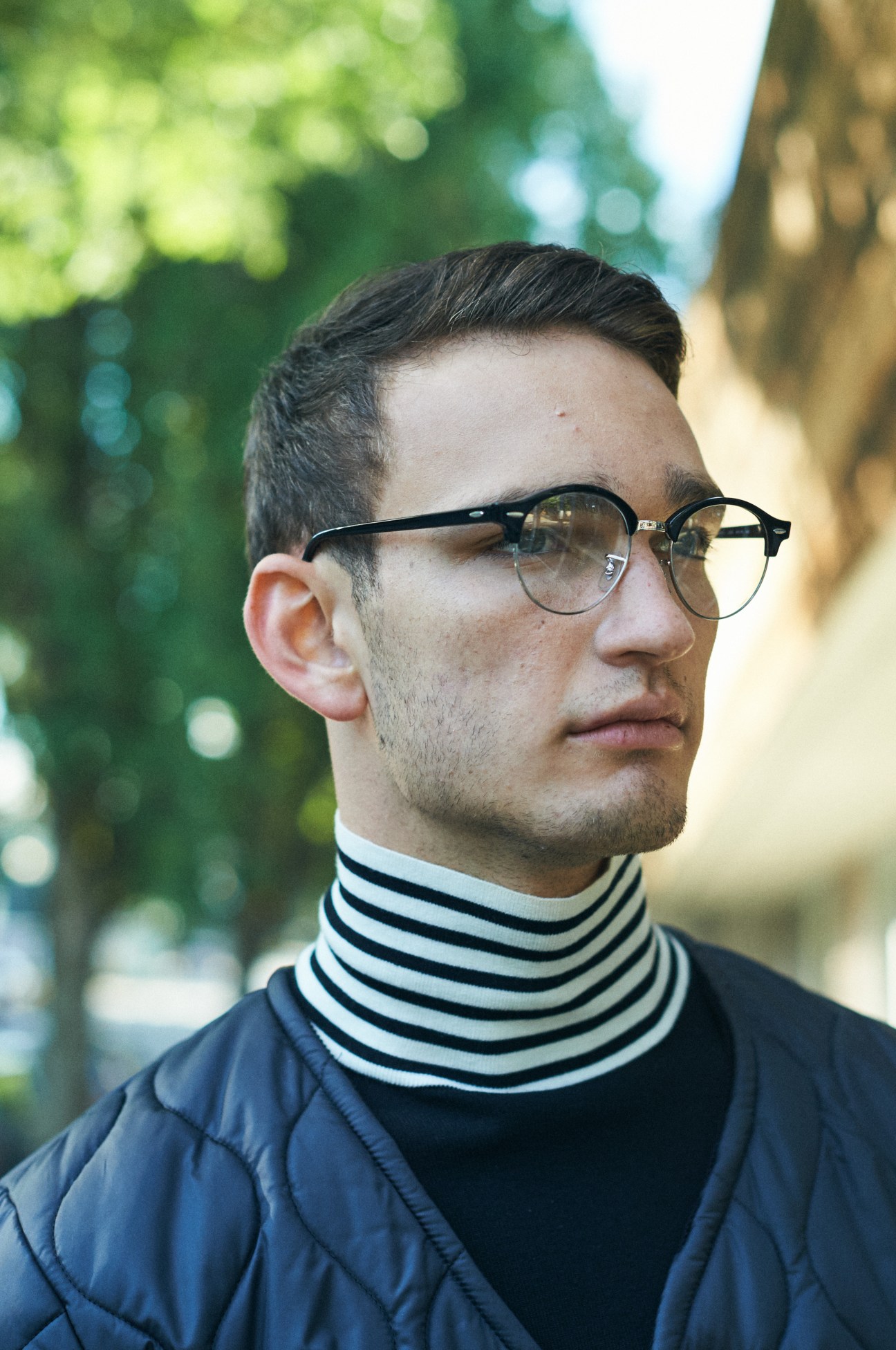 Man in quilted jacket and striped turtleneck wearing glasses outdoors