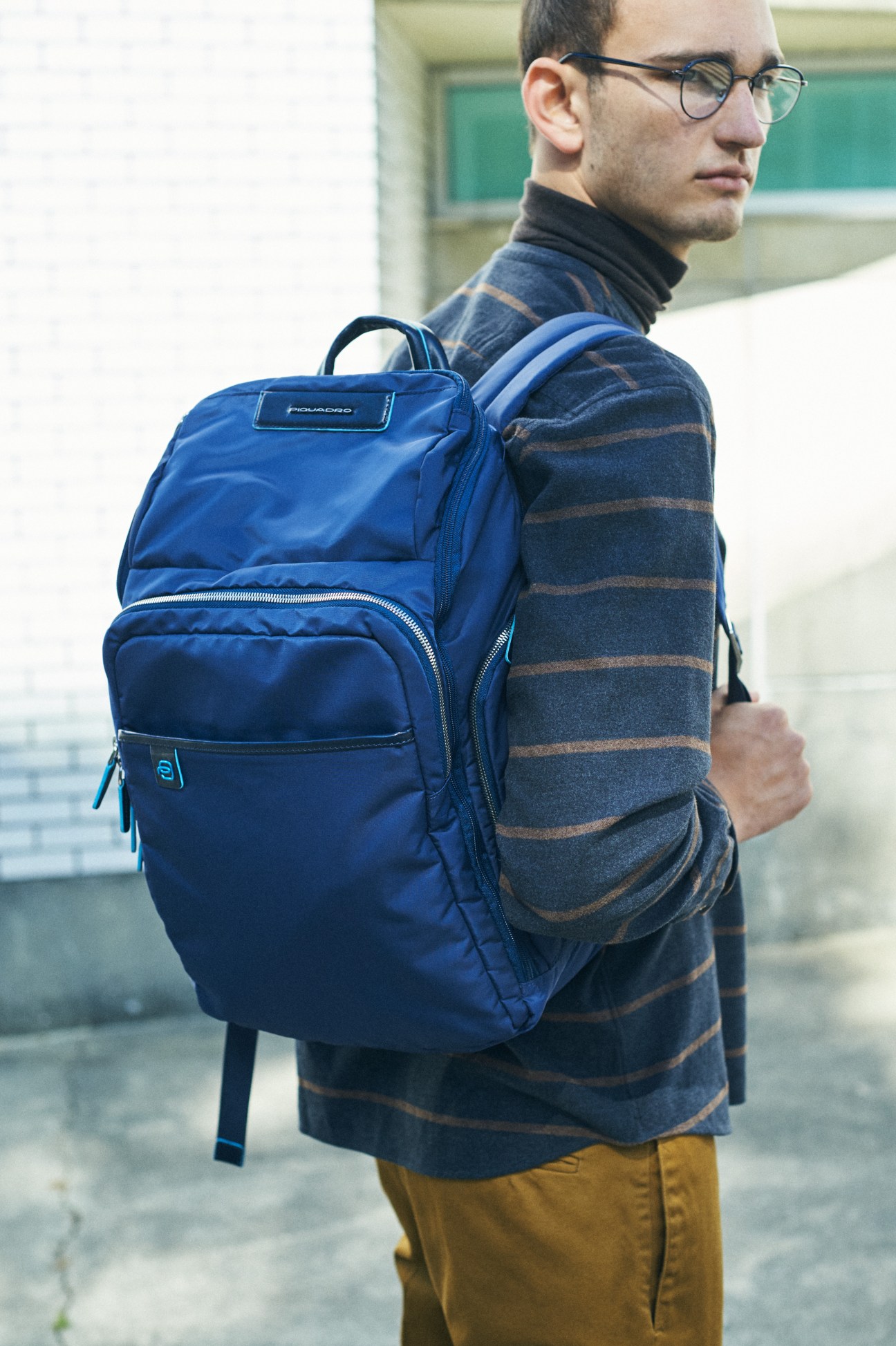 Man wearing glasses and striped rollneck jumper with blue Piquadro backpack