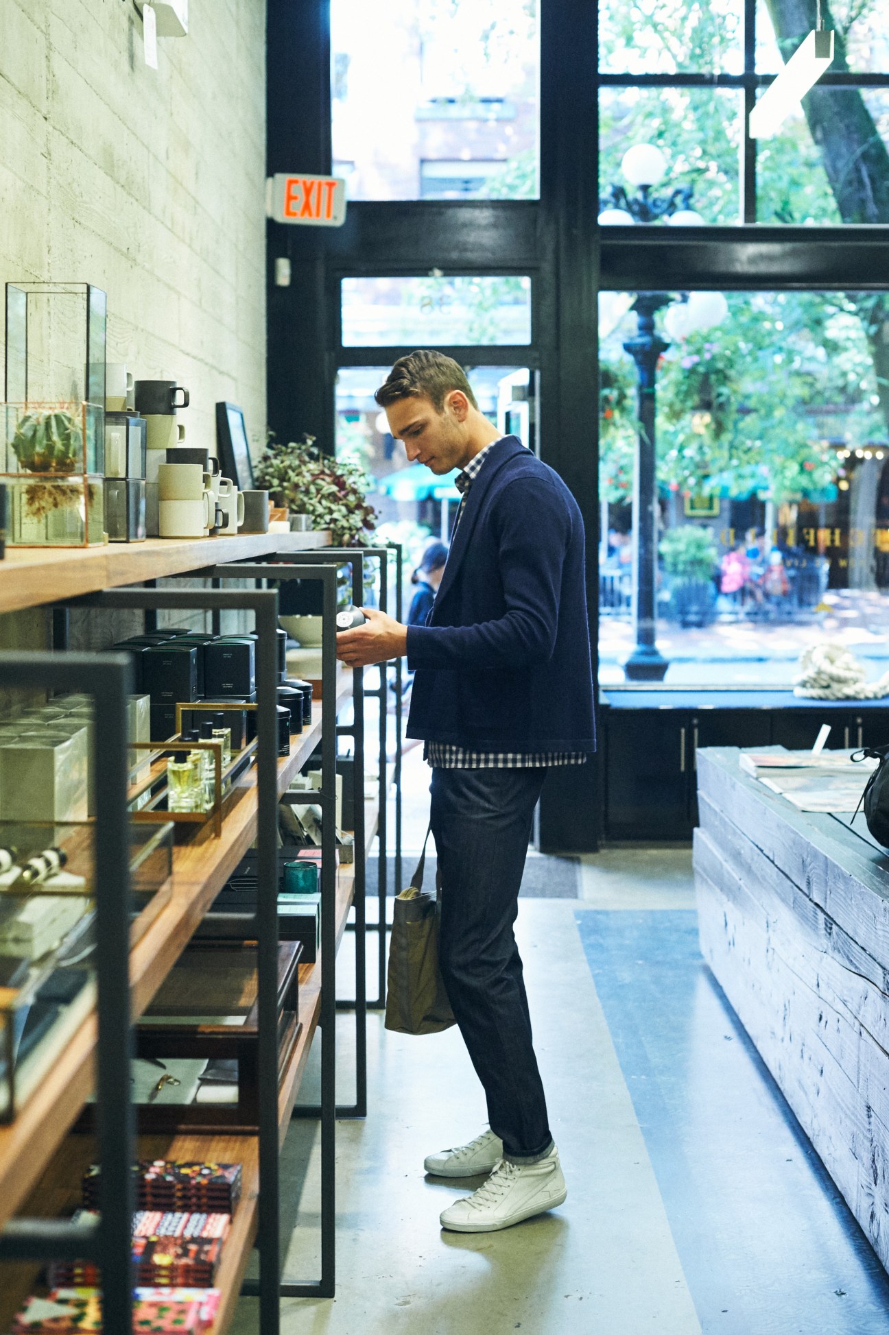 Man in navy jacket examining items on retail shelving in modern store with large windows