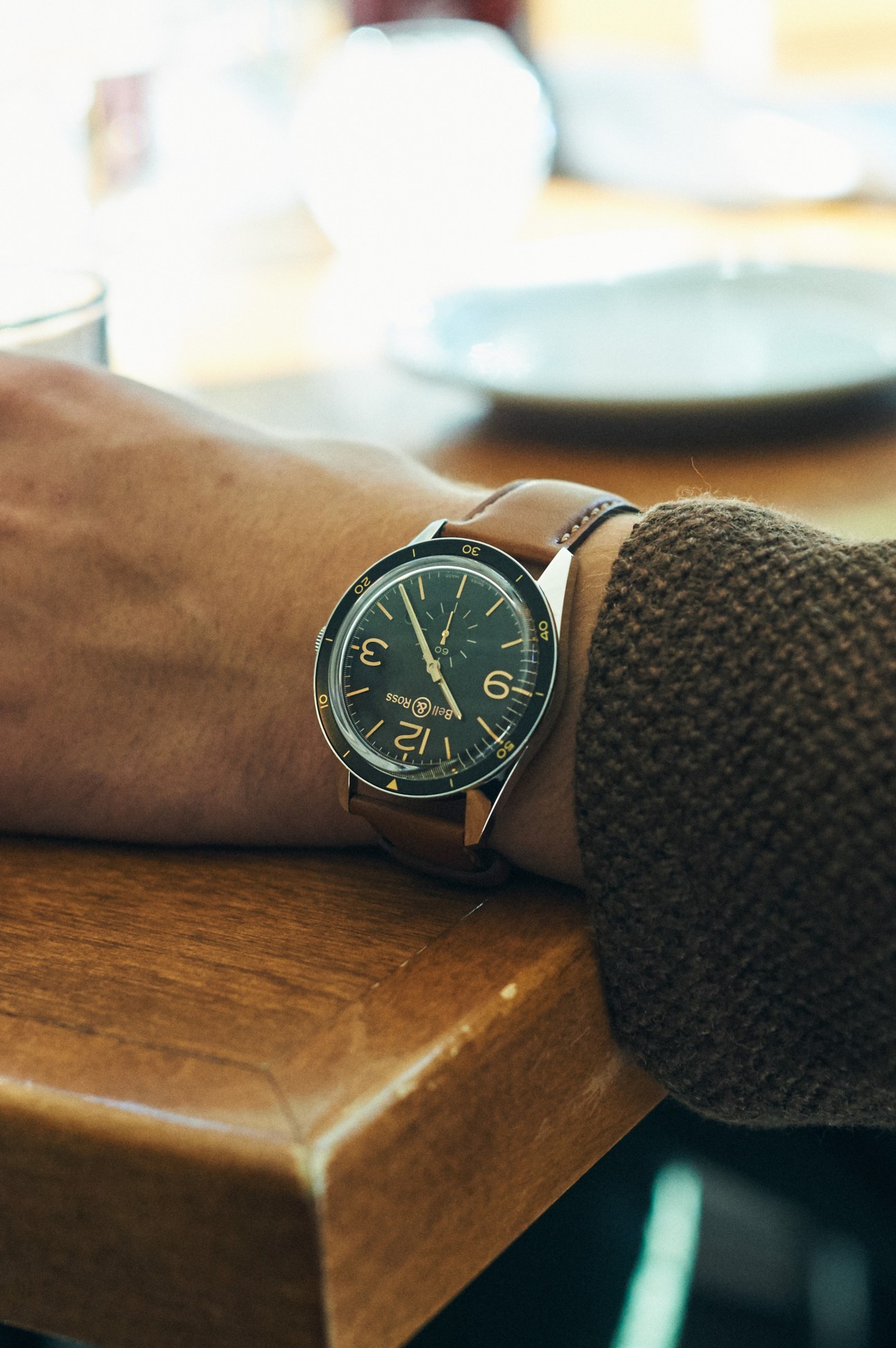 Close-up of a Bell & Ross watch with green dial on man's wrist resting on wooden surface