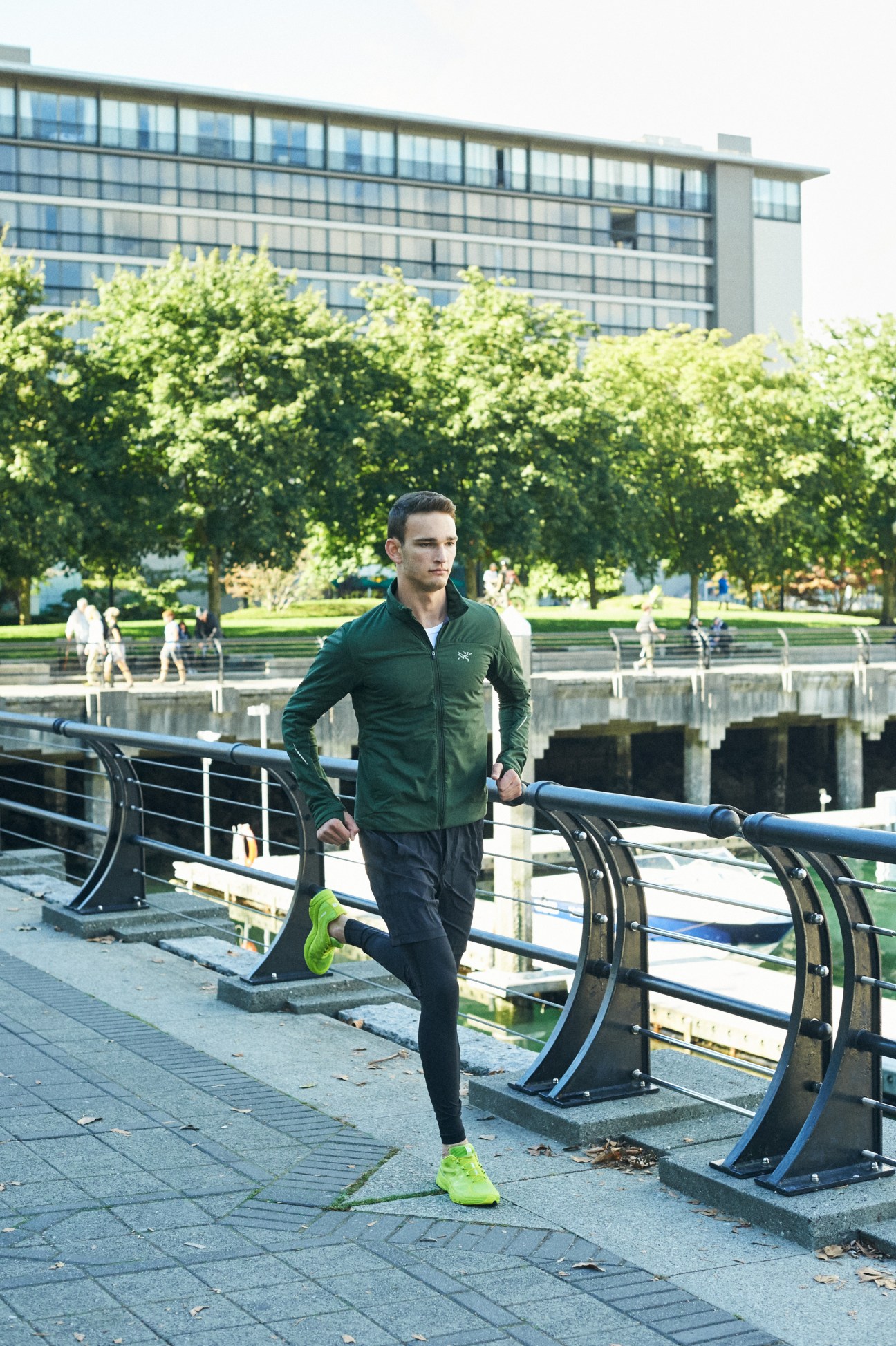 Man running on waterfront path wearing green Arc'teryx jacket with bright green sneakers and dark leggings