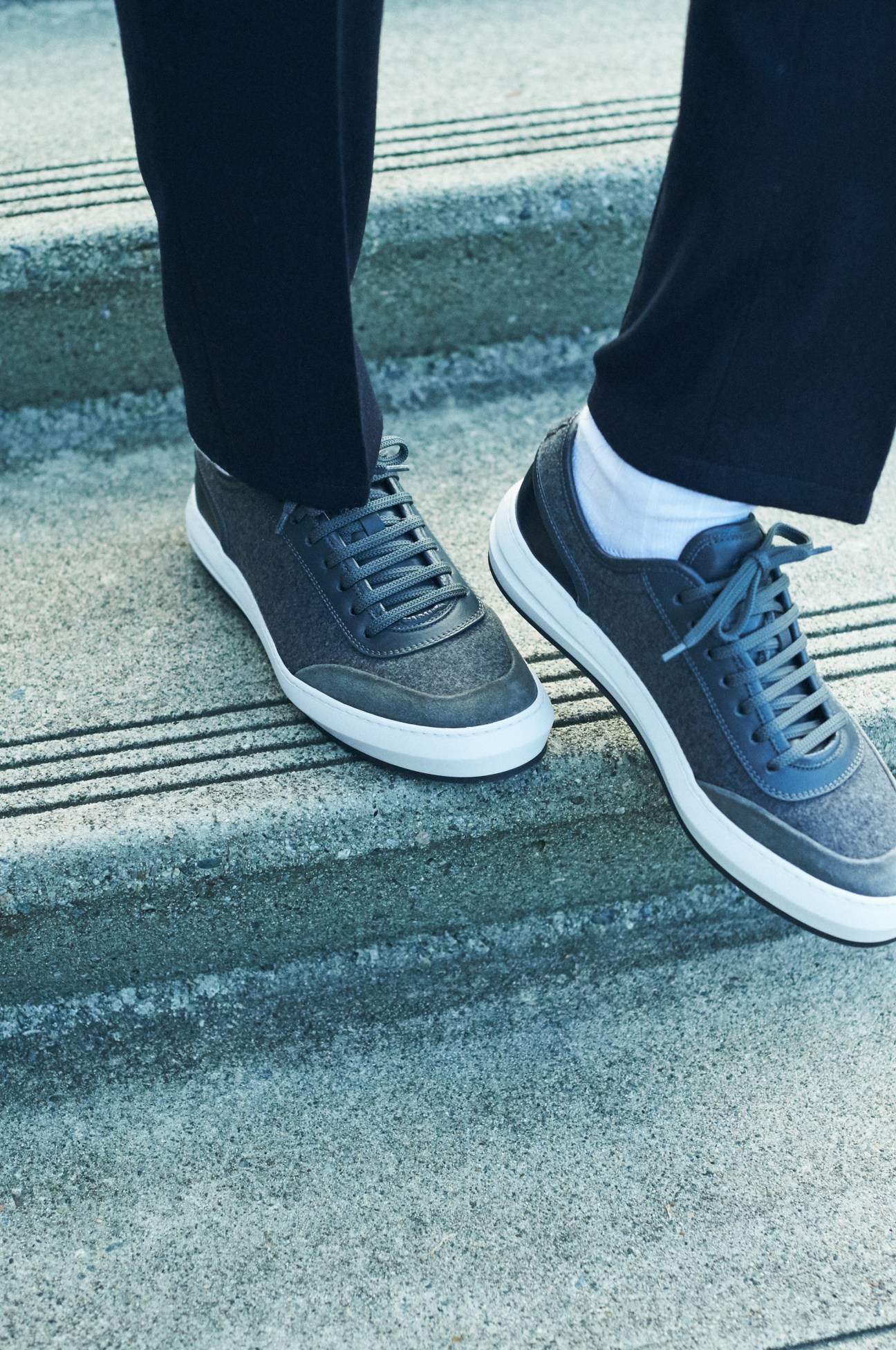 Close-up of feet wearing dark gray Salvatore Ferragamo trainers on concrete steps