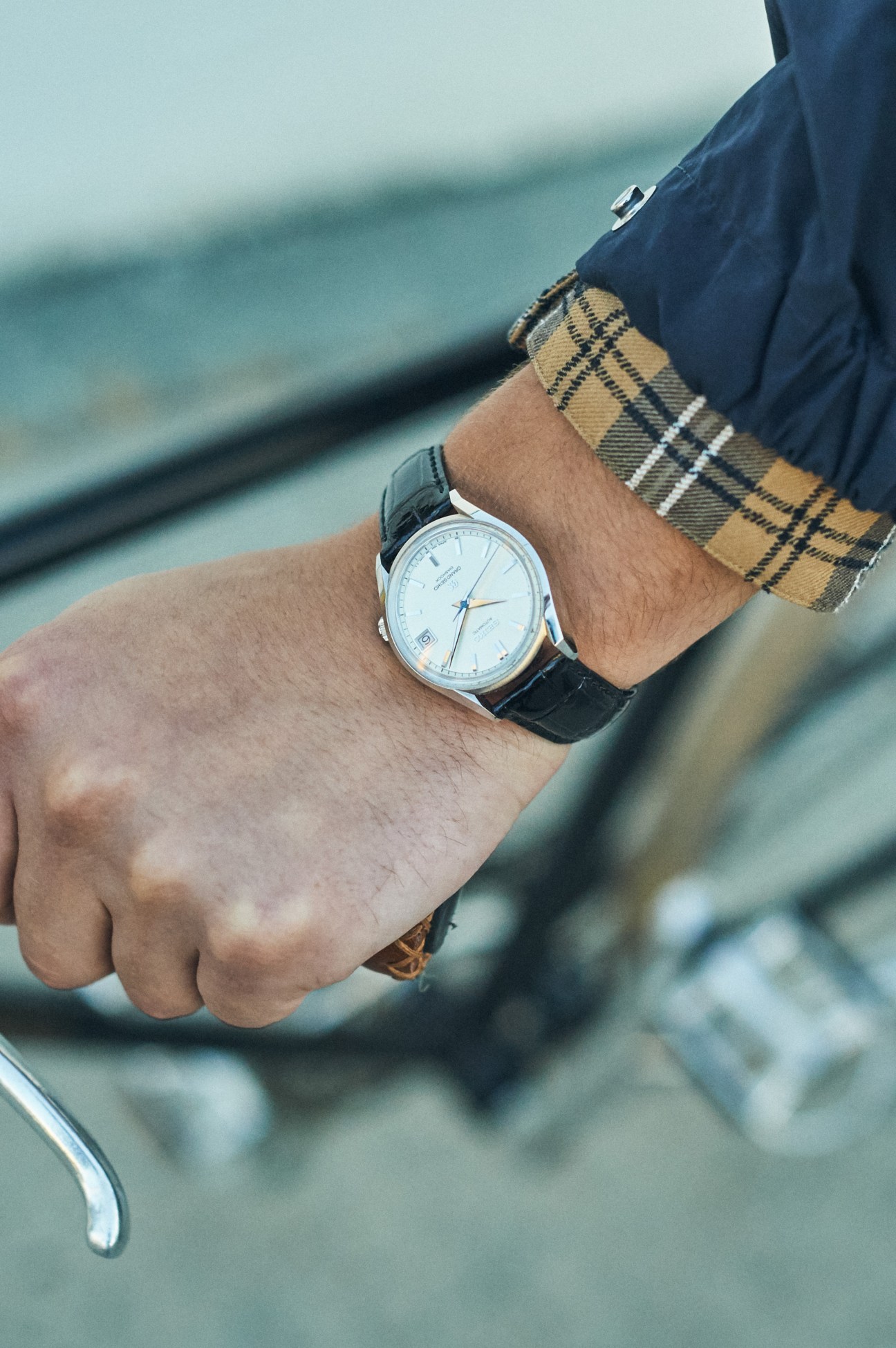 Close-up of a man's wrist wearing a Grand Seiko watch with white dial and black leather strap