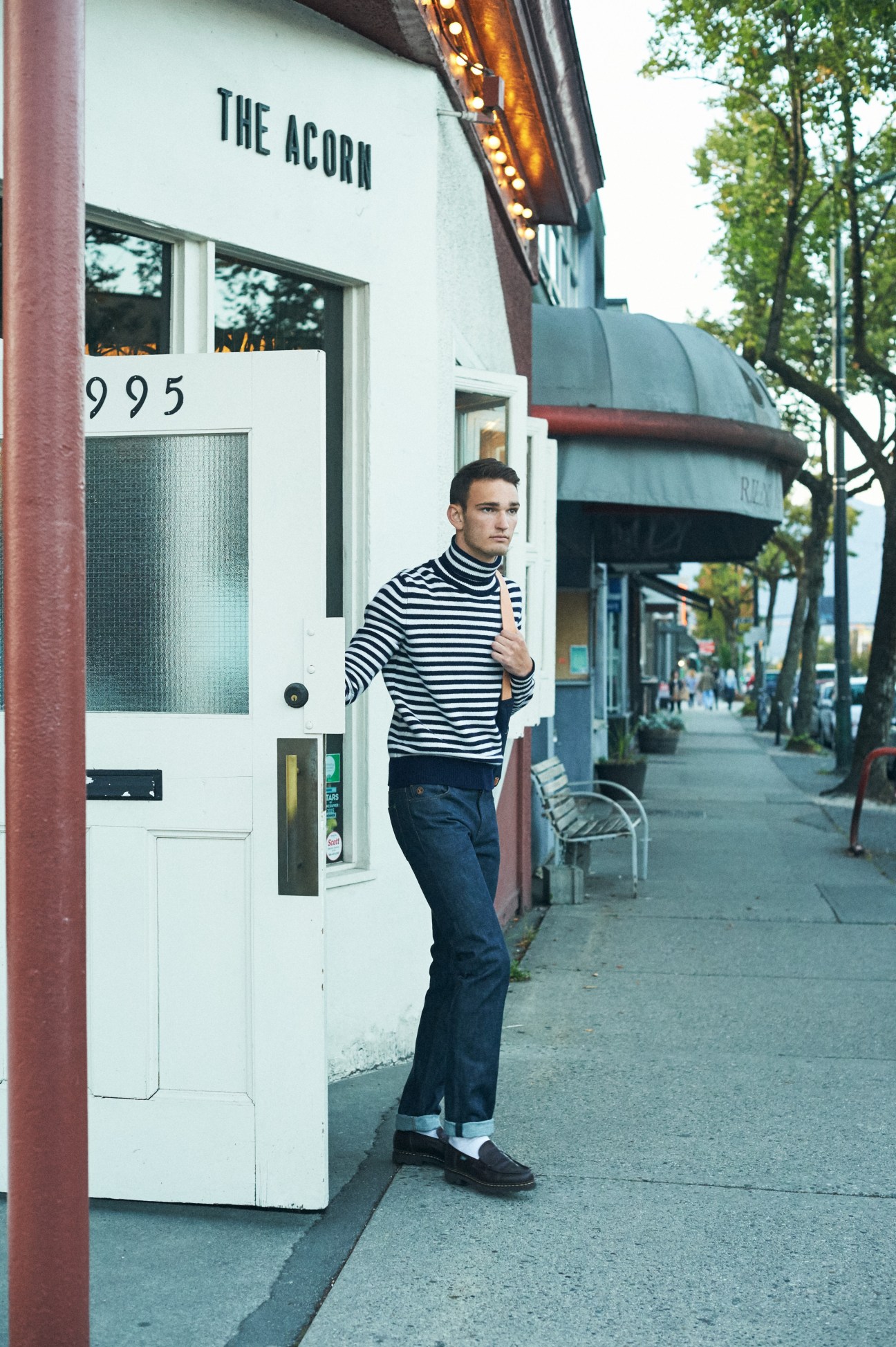 Man in striped turtleneck and jeans standing outside The Acorn restaurant storefront
