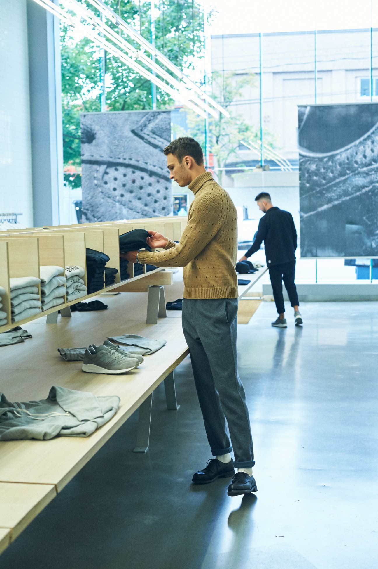 Man in beige turtleneck sweater browsing clothing display in modern retail store with wooden fixtures